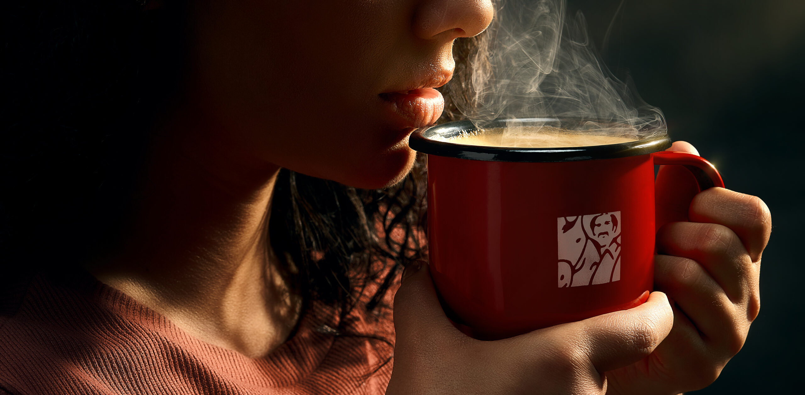 Woman sipping steaming coffee from a red Juan Valdez enamel mug